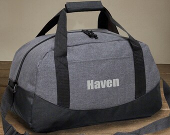 May include: A grey and black duffel bag with a black shoulder strap and a black handle. The bag has the word "Haven" embroidered on the front in white.