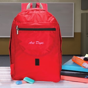 May include: Red backpack with a black zipper and a black pocket on the front. The pocket has the words "Art Dept." embroidered in pink.