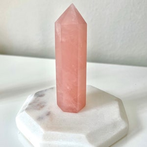 Può includere: Una punta di cristallo di quarzo rosa su una base di marmo bianco.