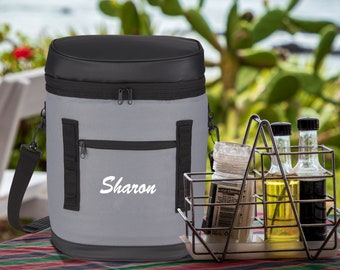 May include: Gray and black insulated cooler bag with a zipper closure and a black shoulder strap. The bag has a front pocket with the name "Sharon" embroidered in white.