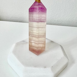 Può includere: Una punta di cristallo a strisce rosa e bianche con un accento dorato in cima, seduta su una base ottagonale bianca.