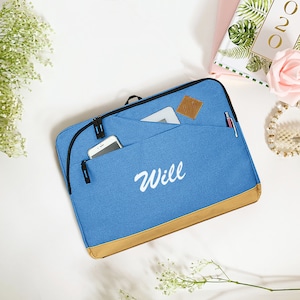 May include: A blue laptop sleeve with a brown trim and a white embroidered name "Will". The sleeve has a zipper closure and a pocket for a phone or other small items.