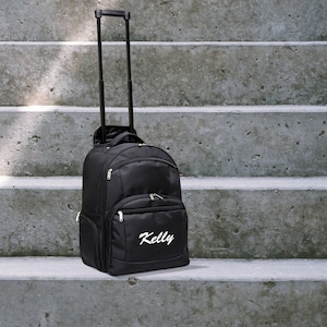 May include: Black rolling backpack with a retractable handle and a white embroidered name "Kelly" on the front.