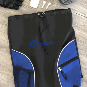 May include: Black drawstring backpack with blue accents, white trim, and the word "Ocean" in blue script. Includes a mesh pocket, a zippered pocket, and a pair of athletic shoes, gloves, and wireless earbuds.