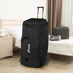 May include: Black rolling duffel bag with a white "Carol" logo on the side. The bag is sitting on a wooden floor in a bedroom setting.