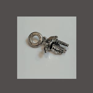 May include: A silver-toned metal charm shaped like a robot with articulated limbs. The circular bail is engraved with the text PANDORA S925 ALE. The charm features a metallic finish with visible joints and a detailed mechanical design throughout the body.