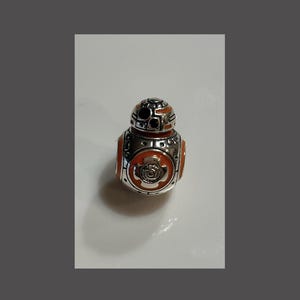 May include: A silver and orange charm shaped like the Star Wars character BB-8.