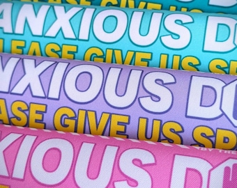 May include: Close-up of four fabric rolls in shades of teal, light blue, lavender, and pink. Each roll displays the words "ANXIOUS DO" in large white letters, with "PLEASE GIVE US SD" in smaller yellow text.