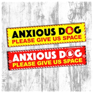May include: Two rectangular signs with the text "ANXIOUS DOG PLEASE GIVE US SPACE". One sign is yellow with black text and a red border, the other is red with white text and a black border. Both signs have a stop hand symbol.