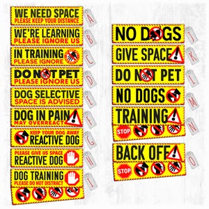 May include: A selection of yellow rectangular signs with black and red text, aimed at dog owners. The signs feature messages such as "We Need Space," "Do Not Pet," and "Reactive Dog," alongside warning symbols. Each sign is accompanied by a tag.