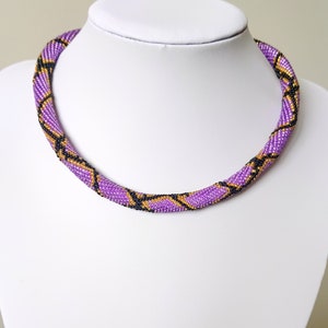 Könnte beinhalten: Eine violette, schwarze und goldene Perlenkette mit Schlangenhautmuster.