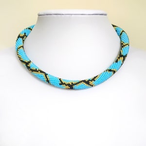 May include: A turquoise, black and gold beaded necklace with a snake skin pattern.