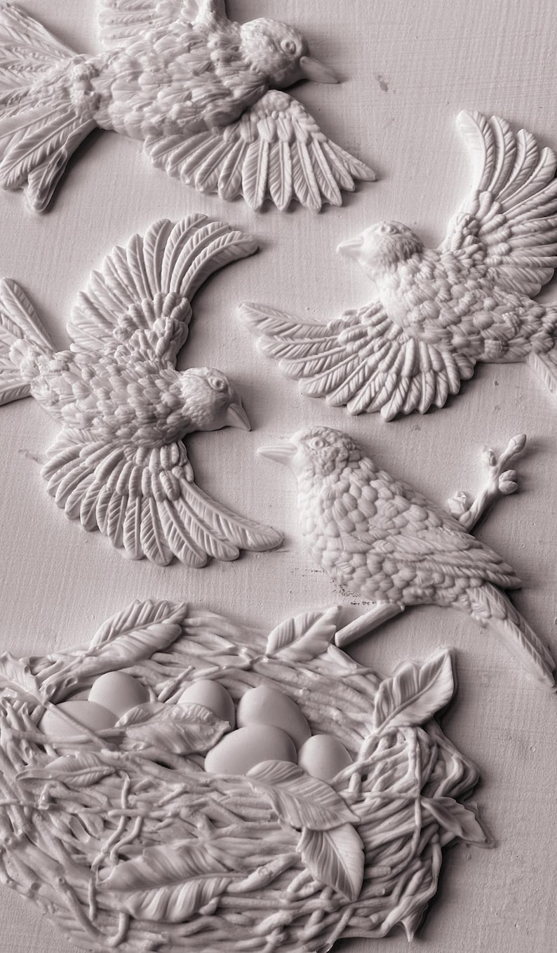 Pode incluir: Escultura em relevo detalhada com v&aacute;rias aves em voo e empoleiradas, juntamente com um ninho contendo ovos. As aves s&atilde;o retratadas com penas e bicos texturizados, e o ninho &eacute; intrincadamente tecido com folhas e galhos. A obra de arte &eacute; monocrom&aacute;tica, esbranqui&ccedil;ada.