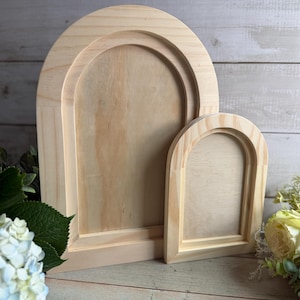 May include: Three unfinished wooden arch-shaped frames of varying sizes. The frames are made of light-colored wood and have a simple, clean design. The largest frame is in the background, with a medium-sized frame in front of it, and a small frame in the foreground.
