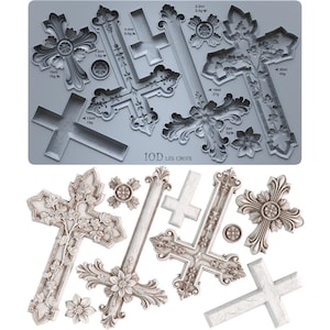 May include: A gray silicone mold featuring various cross designs with floral and ornate details. The mold includes crosses of different sizes, along with the text "IOD LES CROIX" and measurements in milliliters and grams.