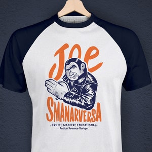 Könnte beinhalten: Ein weißes und marineblaues Baseball-T-Shirt mit einer Cartoon-Illustration eines Mannes mit einem überraschten Ausdruck. Der Text "Joe Smanarversa" ist in Orange auf dem Shirt gedruckt. Der Text "Brutte Maniere Educational - Antica Fornace Design" ist in Schwarz unter der Illustration gedruckt.
