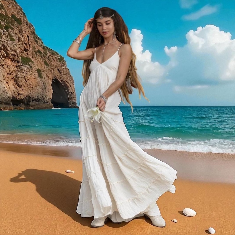 ZinniaPearl’s Savita Wedding Dress is a flowy bohemian gown in soft raw cotton, featuring a plunging neckline, smocked stretch-back waist, and self-tie straps. With a semi-sheer tiered skirt and no lining, it’s ideal for beach weddings or elopements. Designed to flatter a range of sizes including plus, this artisan bridal dress offers natural movement, elegance, and free-spirited beauty.