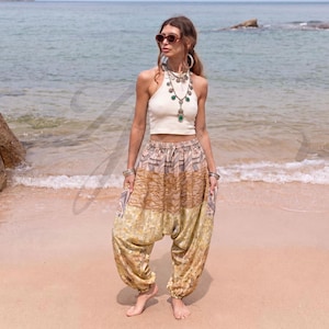 May include: A cream-colored sleeveless crop top paired with loose-fitting harem pants featuring a multi-patterned design in shades of tan, brown, and yellow. The pants have a gathered elastic waistband and cuffed ankles with a drop-crotch silhouette.