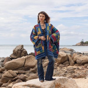 May include: A long-sleeved, open-front jacket featuring a patchwork design of blue, red, yellow, and green fabric squares with white stitched detailing. The garment has a boxy silhouette, wide sleeves, and a mandarin-style collar with toggle closures.