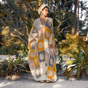 May include: A woman wearing a white and yellow patchwork kaftan with a floral design. The kaftan has a loose fit and long sleeves. The woman is wearing a white head scarf and has long brown hair.