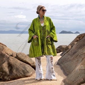 May include: A lime green open-front jacket featuring a subtle dark green patterned print, wide sleeves, and two front patch pockets. The garment is worn over a white top and light-wash distressed denim jeans with frayed hems and large knee rips.