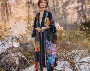 May include: A long, black kimono with a colorful patchwork design. The kimono has a tie closure and is made of a soft, flowing fabric. The model is wearing the kimono with a head scarf and brown boots.