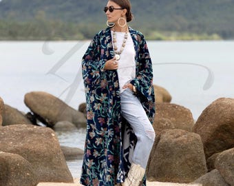 May include: A long, navy blue floral print kimono-style robe. The robe features a colorful floral pattern and is worn over a white top and light blue jeans. The person is wearing sunglasses, large hoop earrings, and white boots.