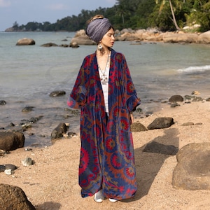 May include: A long, blue and red patterned velvet robe with a shawl collar. The robe is worn by a person standing on a sandy beach.