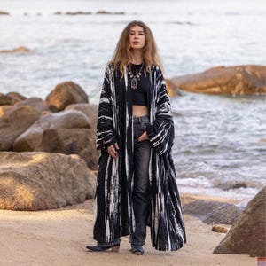 May include: A long, open-front kimono-style robe featuring a black and white tie-dye pattern with vertical stripes. The garment has wide, loose sleeves and a floor-length hem, worn over a black tank top and dark gray denim jeans.