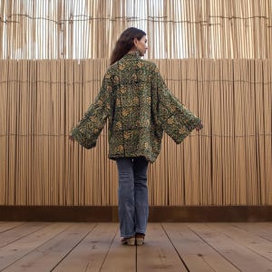 Back view of the emerald floral hand block-printed velvet kimono jacket featuring wide sleeves and relaxed fit, displayed against a warm woven bamboo backdrop.