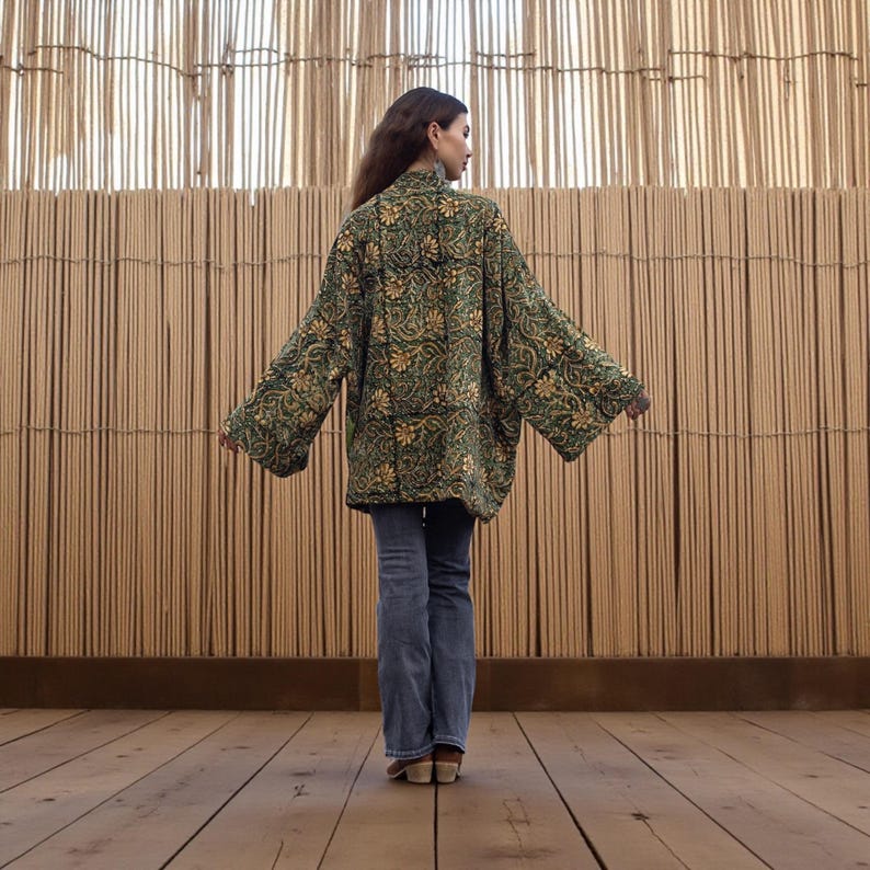 Back view of the emerald floral hand block-printed velvet kimono jacket featuring wide sleeves and relaxed fit, displayed against a warm woven bamboo backdrop.