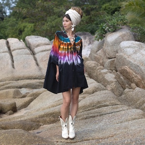 May include: A woman wearing a tie-dye tunic with a black skirt and white cowboy boots. The tunic features a vibrant rainbow pattern on the top and a black skirt. The boots have a star design.