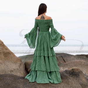 A romantic off-shoulder maxi dress handmade from natural cotton in Elderfern Green, the Lucia Gown features a smocked bodice, tiered ruffle skirt, and vintage-inspired bell sleeves. This breathable and curve-friendly silhouette is ideal for barefoot weddings, sacred ceremonies, maternity photo sessions, or boho festivals. Designed for women who seek soulful elegance, movement, and natural textures.