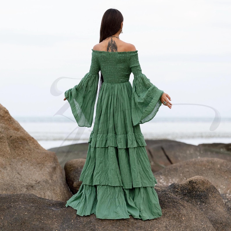 A romantic off-shoulder maxi dress handmade from natural cotton in Elderfern Green, the Lucia Gown features a smocked bodice, tiered ruffle skirt, and vintage-inspired bell sleeves. This breathable and curve-friendly silhouette is ideal for barefoot weddings, sacred ceremonies, maternity photo sessions, or boho festivals. Designed for women who seek soulful elegance, movement, and natural textures.
