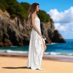 Off-white boho bridal gown crafted from raw cotton, featuring a plunging neckline, smocked back, and tiered skirt. This unlined wedding dress by ZinniaPearl is handmade for destination weddings, elopements, and summer ceremonies. Its flowing fit and natural fabric provide comfort for plus size and standard sizes alike. Lightweight and breathable with an earthy, minimalist charm.