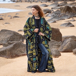 Pode incluir: Um casaco tipo quimono comprido e aberto à frente com um design de patchwork que combina painéis de tecido em verde-azeitona, preto e azul-petróleo com detalhes de costura branca. A peça tem mangas largas e um rebordo em ganga escura.