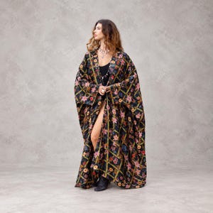 May include: A floor-length, open-front kimono robe featuring a black base with a repeating gold lattice pattern and colorful floral prints in shades of pink, red, and blue. The garment has wide, loose sleeves and a flowing, relaxed silhouette.