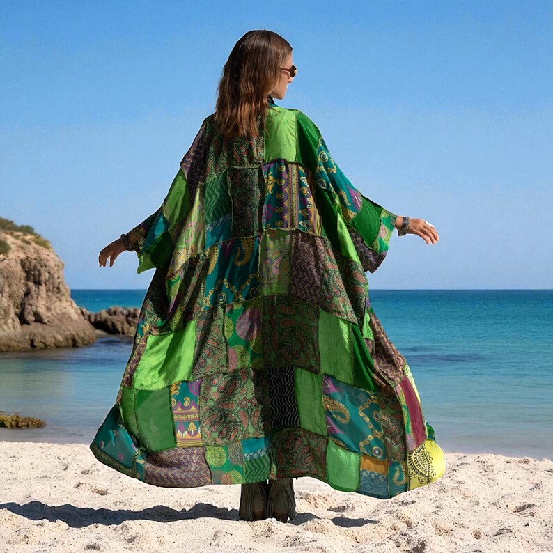 Back view of the Harper Jade Kimono in Emerald Oasis, showing the dramatic patchwork of vintage silk saris in emerald, teal, and patterned squares. Photographed on the beach with the ocean horizon behind, the robe’s wide sleeves and free-flowing drape embody boho goddess style. A unique, handmade duster robe for artisan fashion enthusiasts.