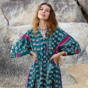 6. Close-up portrait of model wearing the Cora Midi Dress in Peacock Rose featuring dramatic wide sleeves and artisan detailing. The oversized boho midi dress showcases intricate teal floral-inspired print with vibrant magenta accents, relaxed drop shoulders, and flowing cambric cotton fabric. Styled with layered jewelry for an elevated free-spirited bohemian aesthetic.