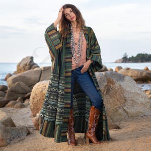 May include: A long, green, and brown patterned cardigan with a striped design. The cardigan is worn over a peach colored tank top and blue jeans. The person is wearing brown cowboy boots.