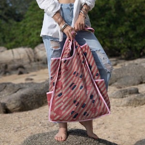 Model holding the Kaia Dusty Rose Polka Kantha hobo bag, a reversible vintage quilt shoulder tote handcrafted from upcycled cotton sari textiles. The soft dusty rose base features diagonal stripe texture with polka-inspired detailing and hand-stitched Kantha running stitch, styled casually with denim against a rocky outdoor backdrop.