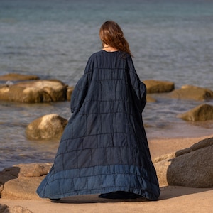 Back view of the Midnight Indigo blue robe. The patchwork construction is clearly visible, with a subtle design detail at the hem where a lighter blue panel creates a two-tone effect. The maxi length creates a sweeping, dramatic exit.