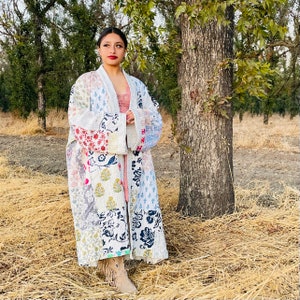 May include: A white quilted robe with a floral patchwork design. The robe has a long, flowing silhouette and is perfect for layering over clothing.