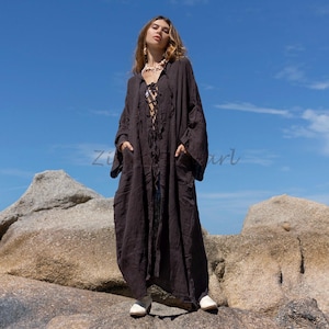 May include: A long, black, hooded robe with a lace-up front and pockets. The robe is made of a soft, flowing fabric and is worn by a person standing on a rocky surface.