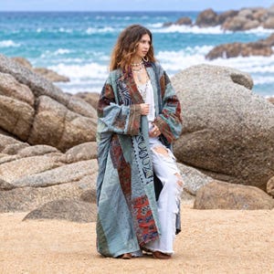 May include: A long, open-front kimono-style robe featuring a patchwork design with various blue, grey, and rust-colored patterned fabric panels. The garment is worn over a white top and distressed white denim jeans with large knee-area rips.