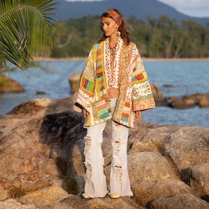 May include: A colorful patchwork kimono-style jacket with a variety of patterns and colors, including orange, yellow, and blue. The jacket is paired with ripped, light-wash jeans. A matching headband and jewelry complete the look.