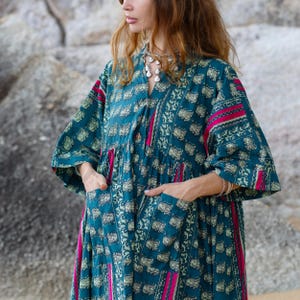 7. Detailed close-up of the Cora Midi Dress in Peacock Rose highlighting deep pockets, soft cotton texture, and artisan print details. The relaxed oversized silhouette features wide kimono sleeves, gathered neckline, and teal floral-inspired motifs contrasted by vibrant magenta accents. The lightweight cambric cotton drapes effortlessly for comfortable boho styling and elegant movement.