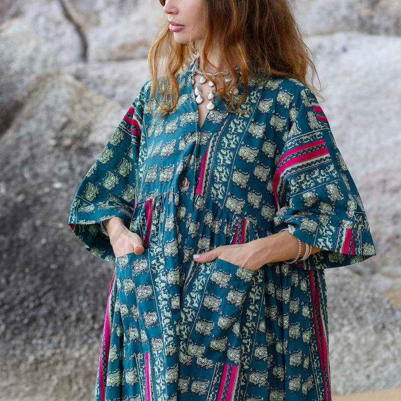 7. Detailed close-up of the Cora Midi Dress in Peacock Rose highlighting deep pockets, soft cotton texture, and artisan print details. The relaxed oversized silhouette features wide kimono sleeves, gathered neckline, and teal floral-inspired motifs contrasted by vibrant magenta accents. The lightweight cambric cotton drapes effortlessly for comfortable boho styling and elegant movement.