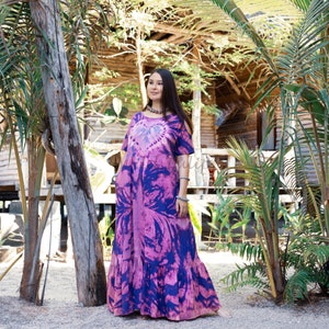 May include: A woman wearing a purple and pink tie-dye maxi dress with a heart design. The dress has a ruffled hem and is made of a soft, flowing fabric.