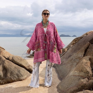 May include: A pink patchwork kimono-style jacket with long sleeves and a tie closure. The jacket features various patterned fabric patches and two front pockets. The person is wearing light-wash, ripped jeans and sunglasses.